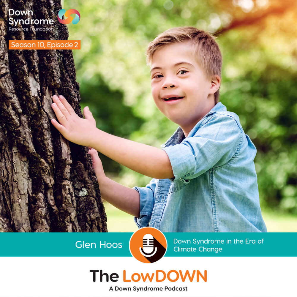 blonde haired white boy with Down syndrome wearing short sleeved blue shirt stands with his hands on a tree