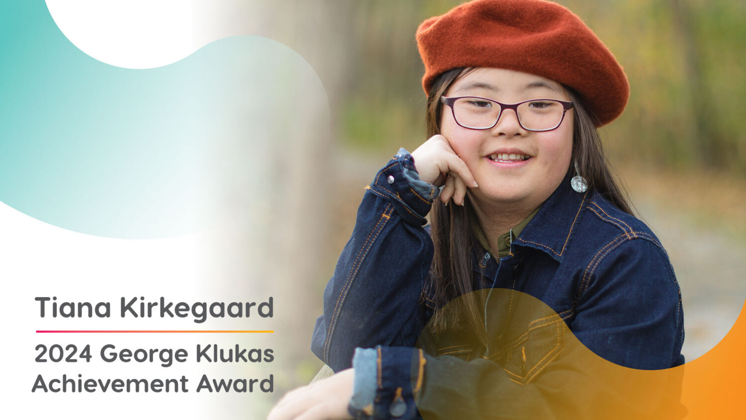 Asian woman with Down syndrome, with long dark hair, glasses, a dark orange hat and a jean jacket, poses outdoors