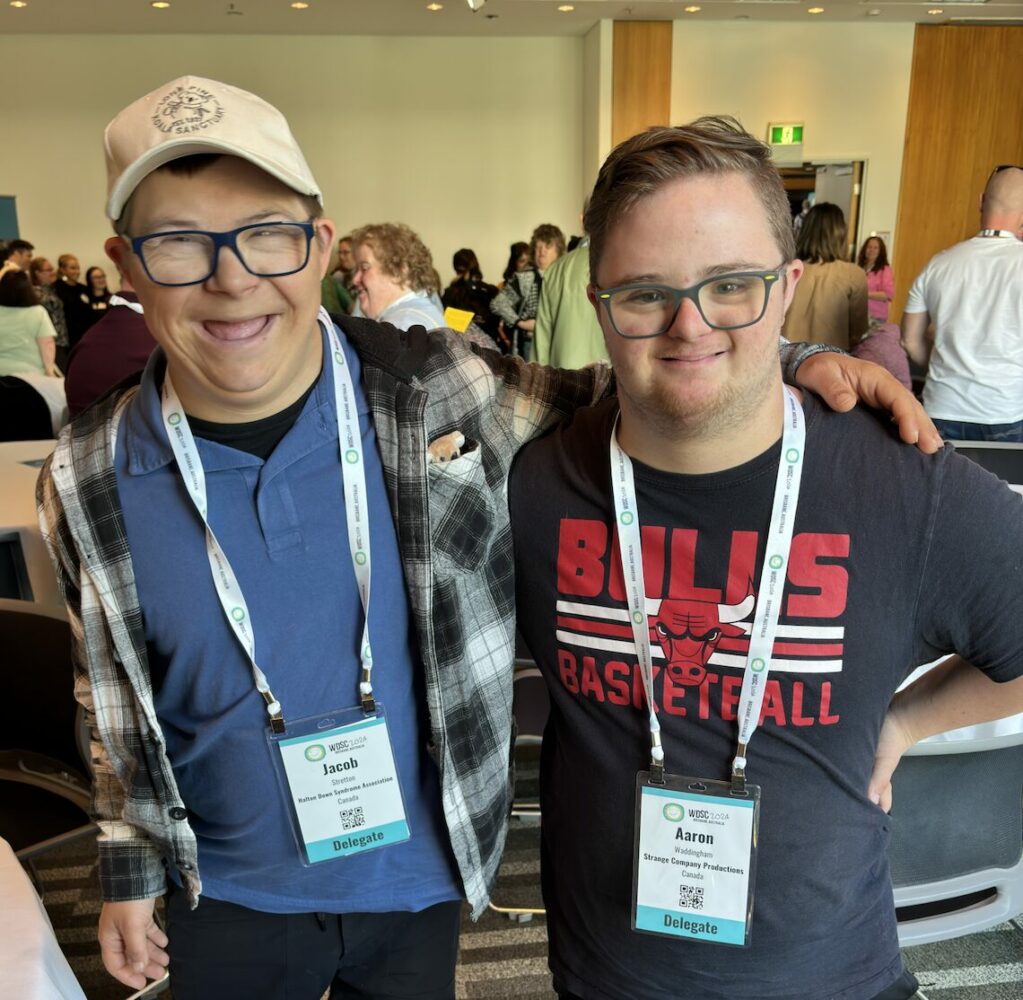 two white men with Down syndrome with lanyards around their necks identifying them as participants at the World Down Syndrome Congress