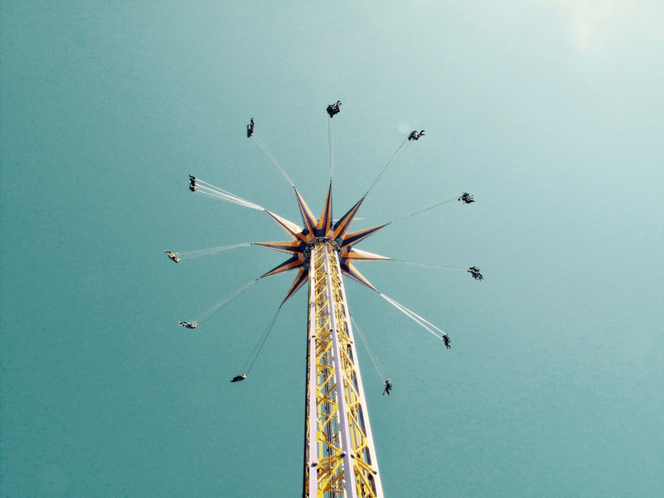 a photograph looking upwards at the swing ride at Vancouver's Playland; a large thin tower with a star atop it and a dozen seats outstretched against a clear blue sky